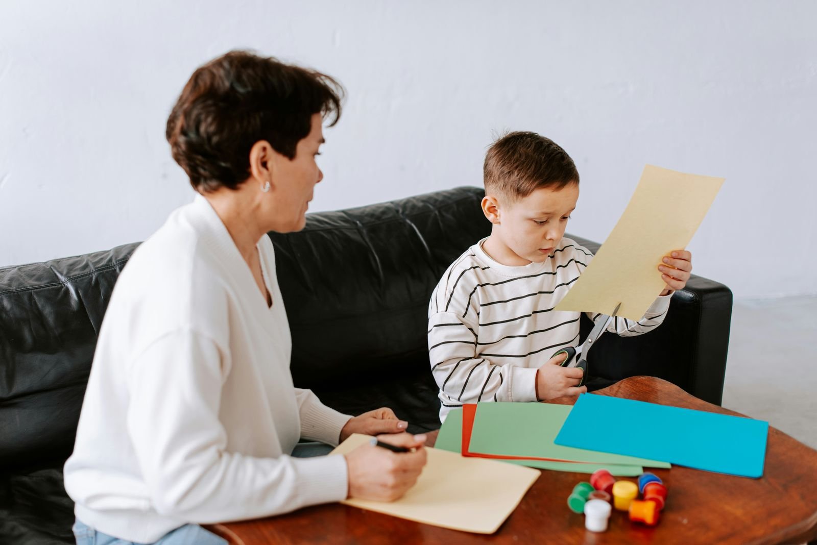 A behavior technician and a young boy work together on a craft activity at home